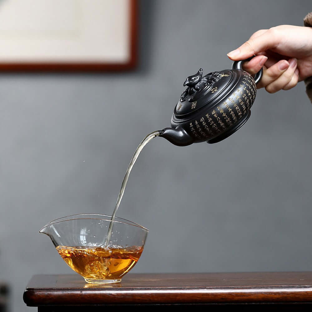 Handmade Yixing purple sand teapot pouring tea into a glass cup, showcasing artistry in traditional tea brewing.
