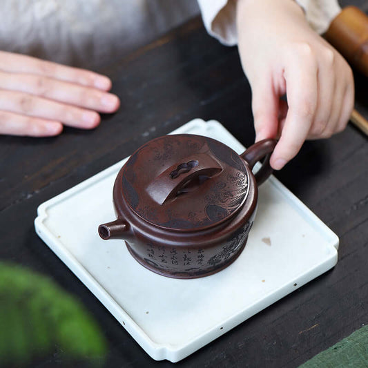 Handmade Yixing purple sand teapot with a lid on a white tray, held by a hand, showcasing craftsmanship and elegance.
