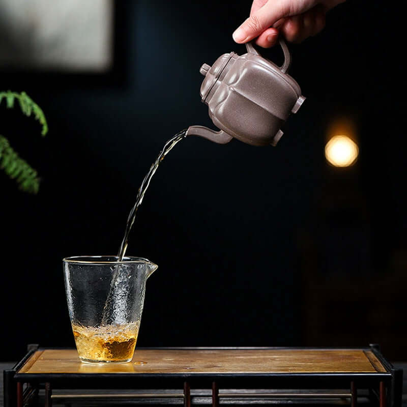 Handmade Yixing purple sand teapot pouring tea into a glass cup, showcasing traditional craftsmanship.