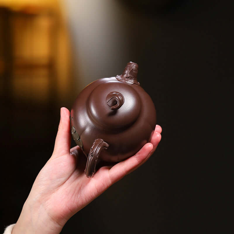 Handmade Yixing purple sand teapot held in hand, showcasing its unique design and craftsmanship.