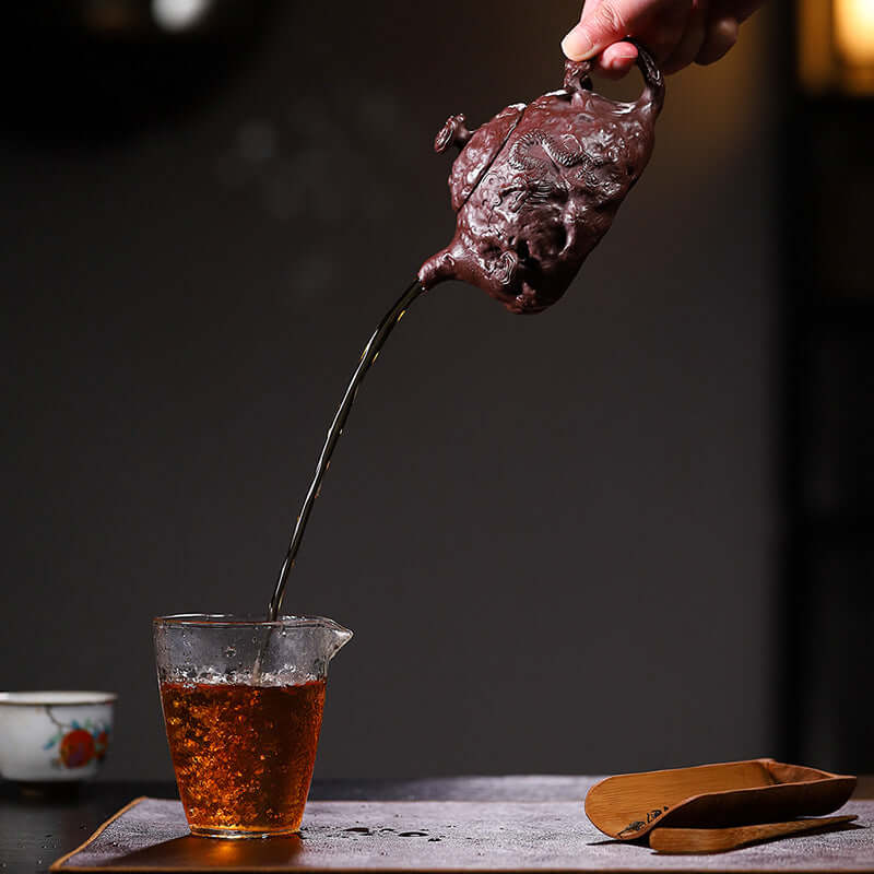 Handmade Yixing purple sand teapot pouring tea into a glass cup, showcasing original craftsman quality and elegance.