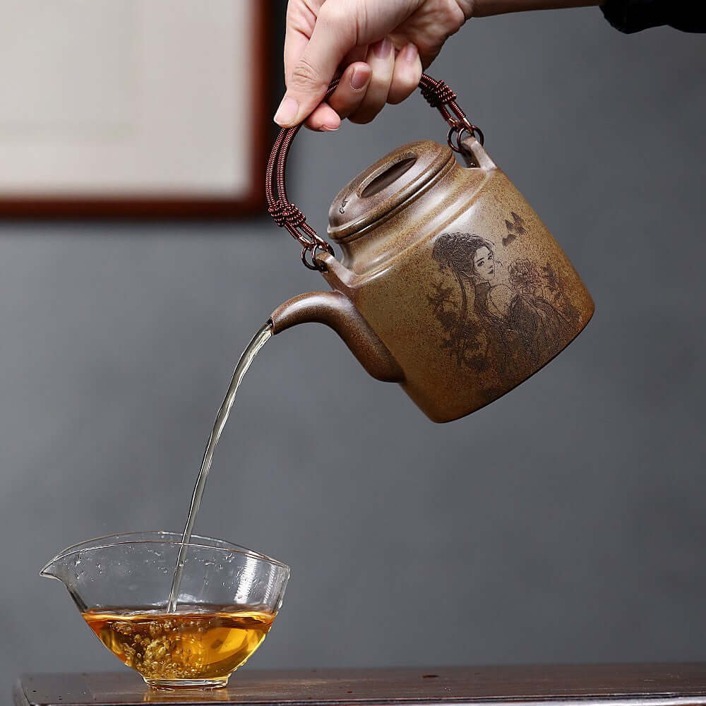 Handmade Yixing purple sand teapot pouring tea into a glass cup, showcasing traditional craftsmanship and elegance.