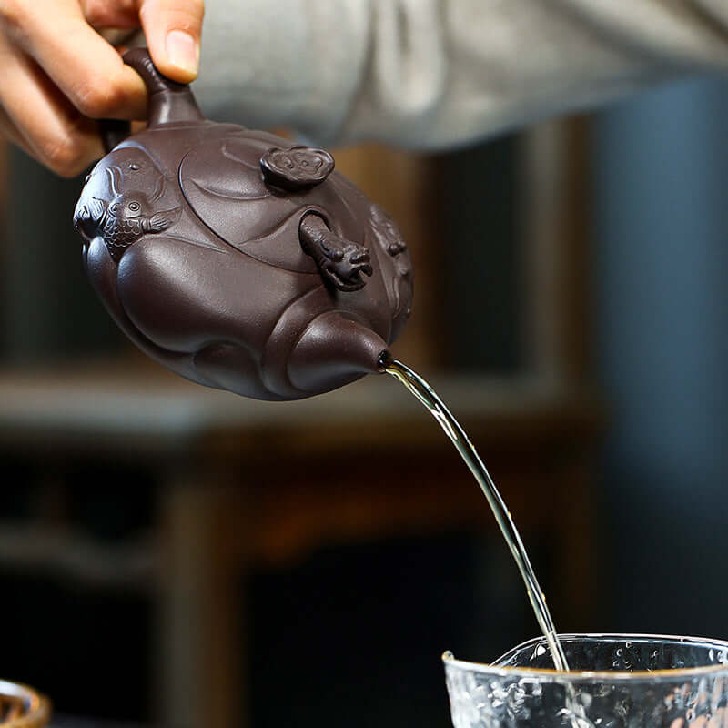 Handmade Yixing purple sand teapot pouring tea from an intricately designed fish dragon teapot.