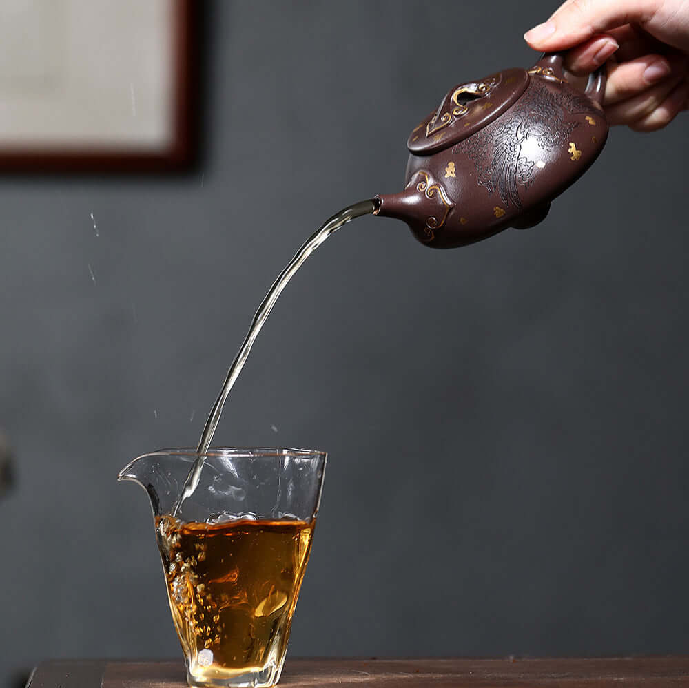 Handmade Yixing purple sand teapot pouring tea into glass cup, showcasing traditional craftsmanship and design.