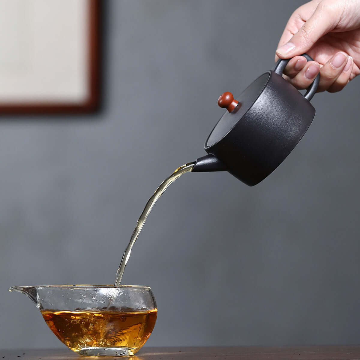 Handmade Yixing purple sand teapot pouring tea into a glass cup, showcasing traditional kung fu tea brewing.