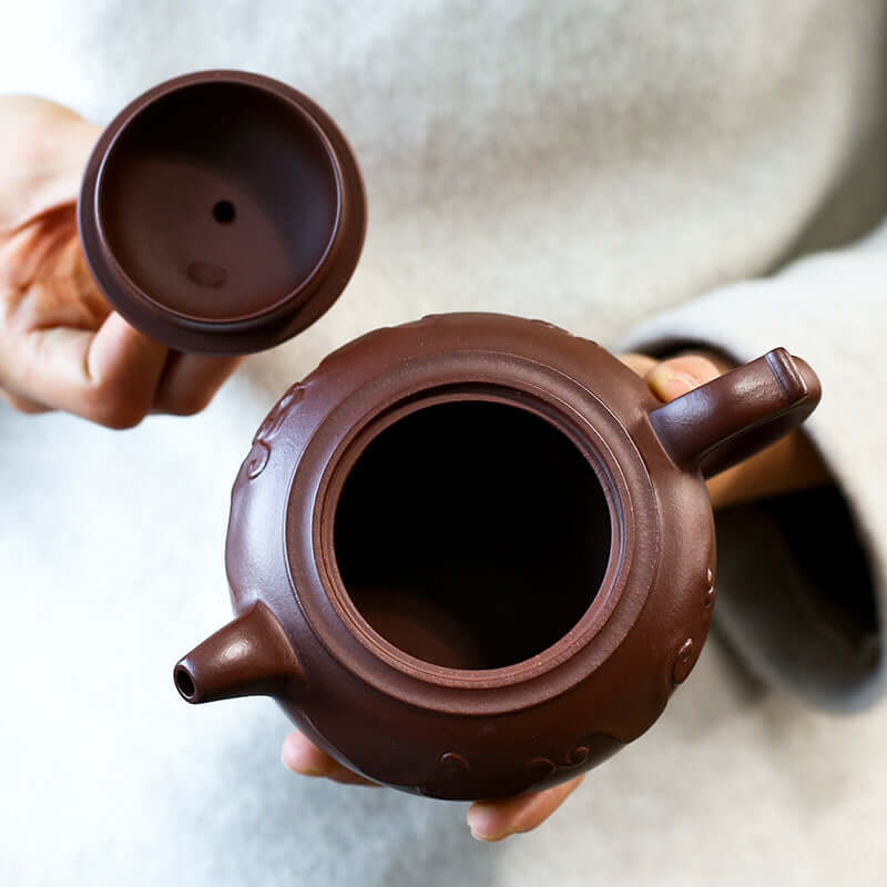 Handmade Yixing purple sand teapot with lid held by artisan, showcasing elegant design and craftsmanship.