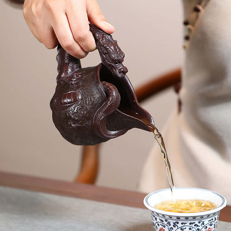 Handmade Yixing purple sand teapot with dragon design pouring tea into a cup, showcasing traditional Chinese craftsmanship.