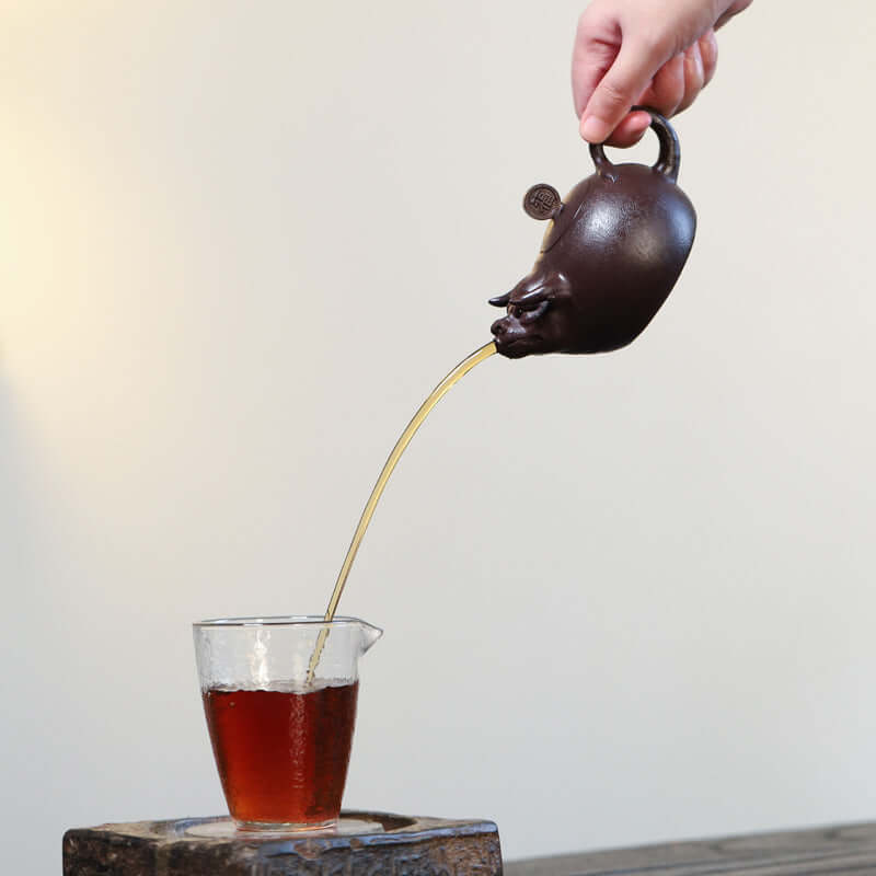 Handmade Yixing purple sand teapot pouring hot tea into a glass cup, showcasing traditional craftsmanship.