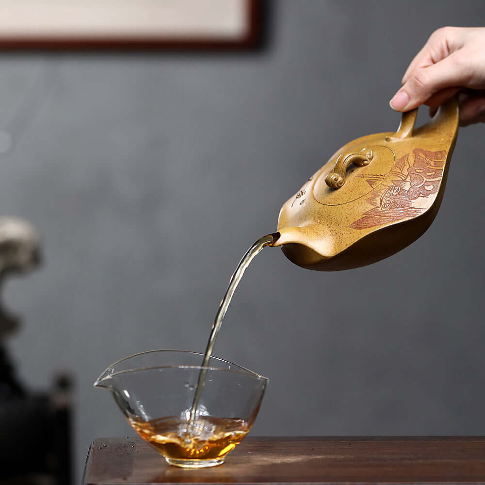Handmade Yixing purple sand teapot pouring tea into a glass cup, showcasing craftsmanship and elegance.