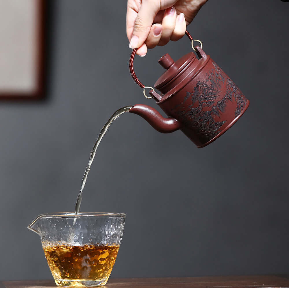 Handmade Yixing purple sand teapot pouring tea into glass cup, showcasing craft and elegance in kung fu tea set.