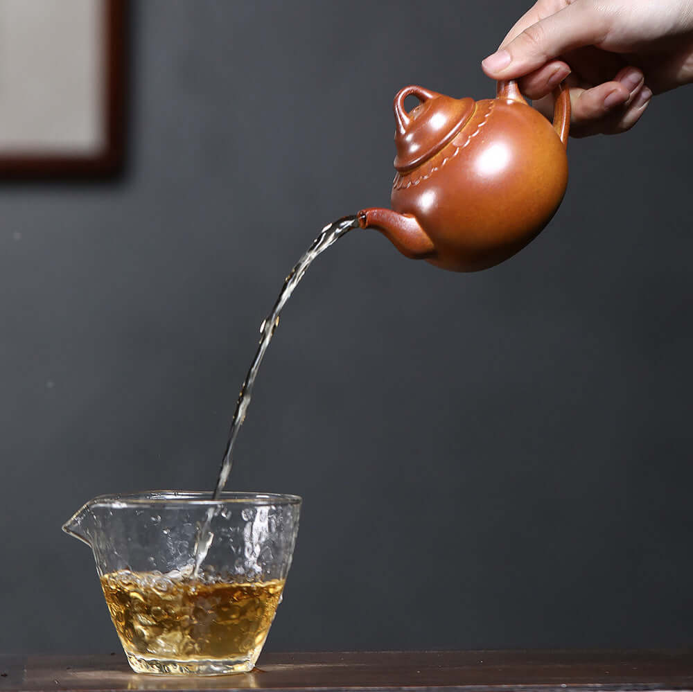 handmade Yixing purple sand teapot pouring tea into a glass cup, perfect for kung fu tea ceremonies