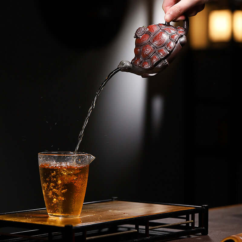 Handmade Yixing purple sand teapot in tortoise shape pouring tea into a glass cup, showcasing original craftsmanship.