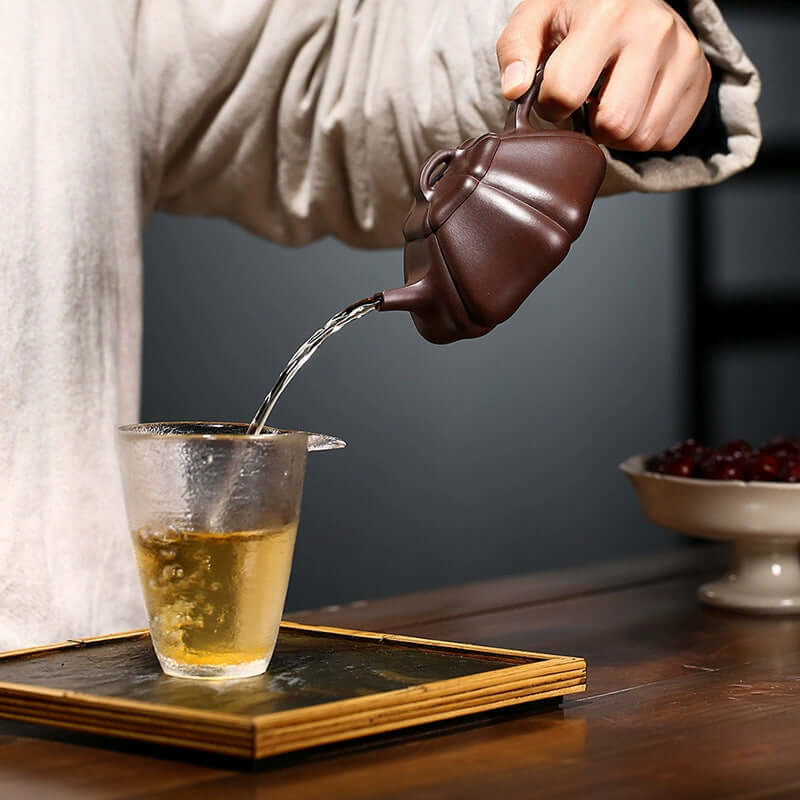 Handmade Yixing purple sand teapot pouring tea into a glass cup, showcasing traditional craftsmanship.
