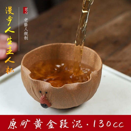 Handmade Yixing golden Duan clay tea cup being filled with tea, showcasing unique craftsmanship and elegant design.