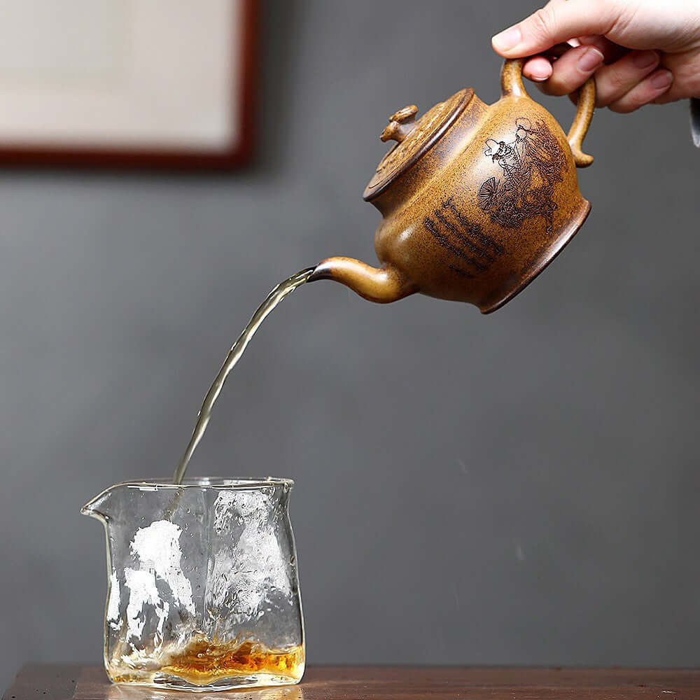 Handmade Yixing purple sand teapot pouring tea into a glass cup, showcasing intricate craftsmanship and design.