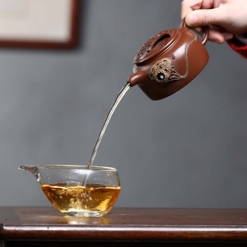 Handmade Yixing purple sand teapot pouring tea into a glass cup, showcasing fine craftsmanship and traditional tea art.