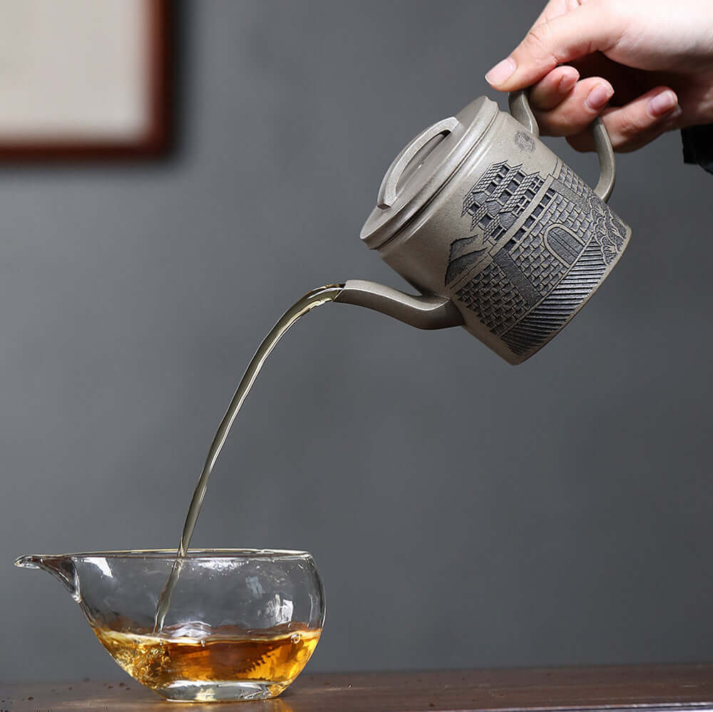 Handmade Yixing purple sand teapot pouring tea into glass cup, showcasing unique craftsmanship and traditional design.