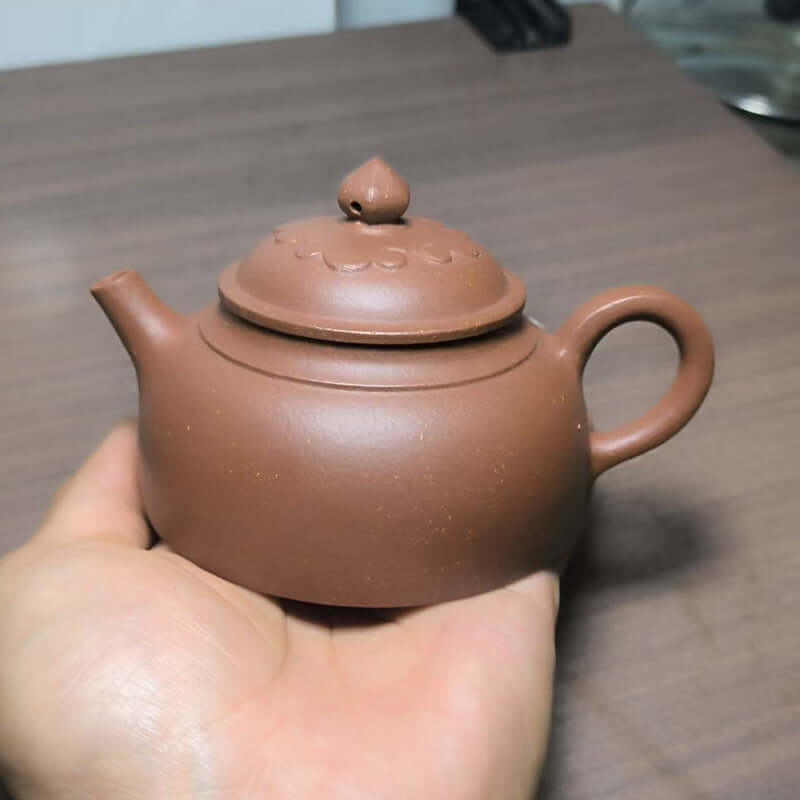 Handmade Yixing purple sand teapot held in hand, showcasing original purple clay craftsmanship.