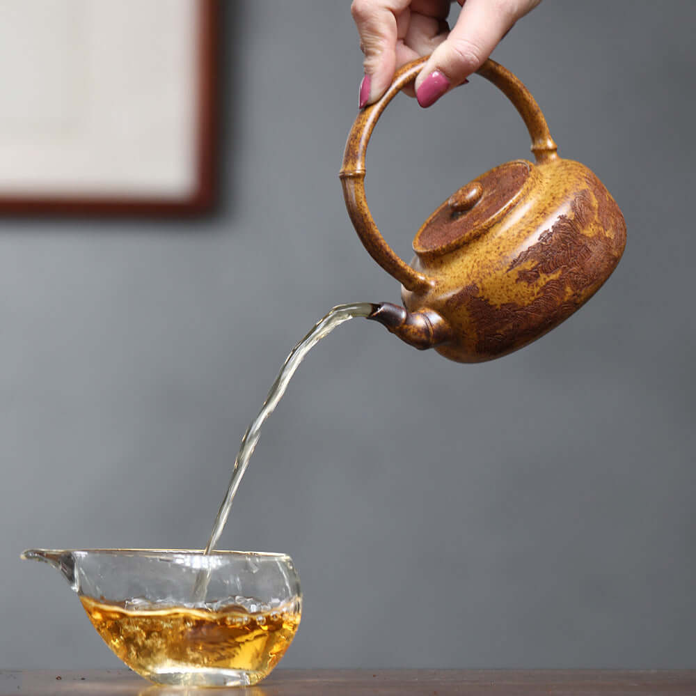 Handmade Yixing purple sand teapot pouring tea into glass cup, showcasing craftsmanship and elegance in kung fu tea set.