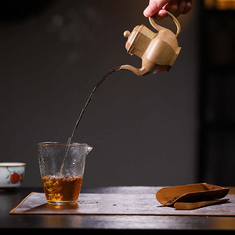 Handmade Yixing purple sand teapot pouring tea into a glass cup, showcasing traditional craftsmanship and elegance.