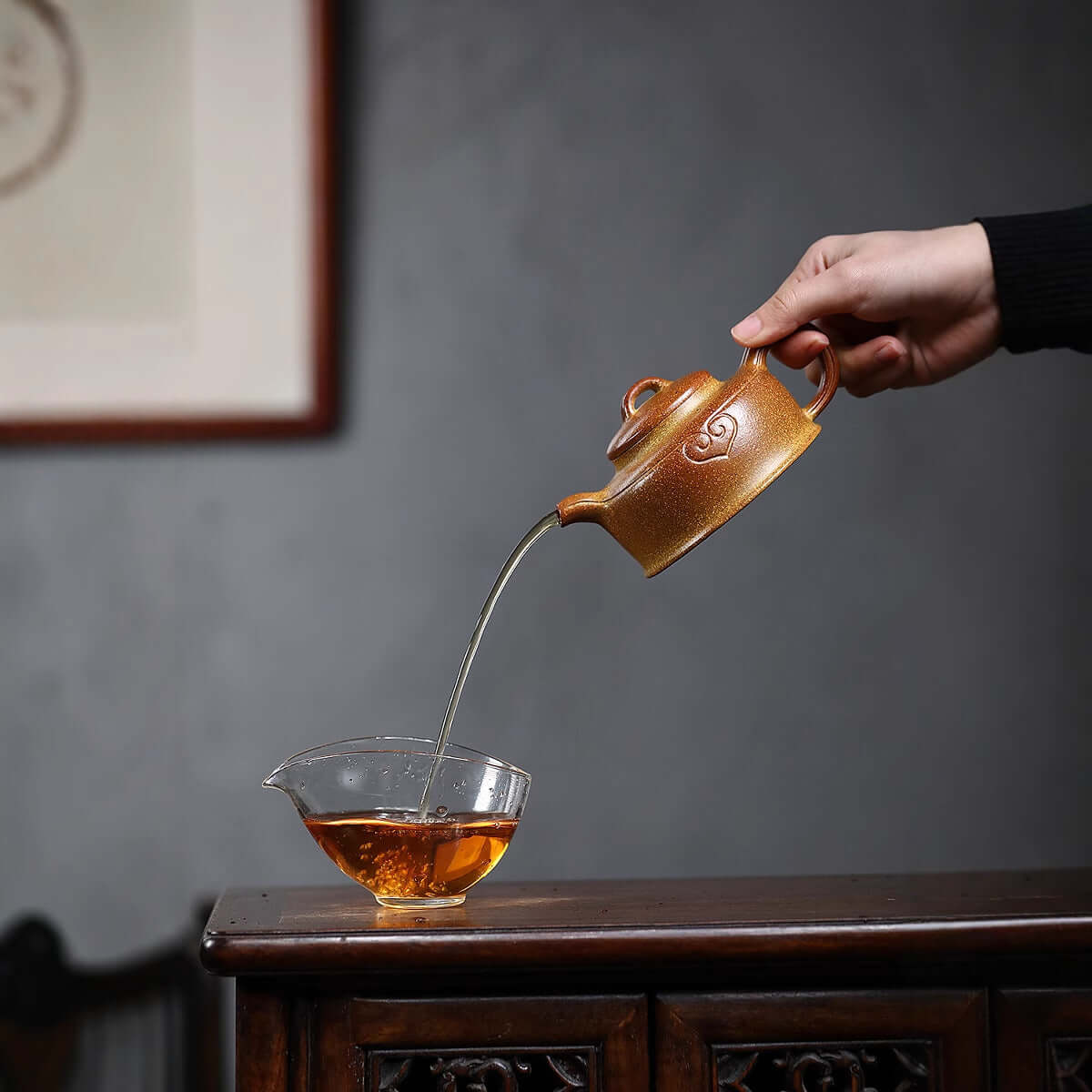 Handmade Yixing purple sand teapot pouring tea into a glass, showcasing traditional craftsmanship and elegance.