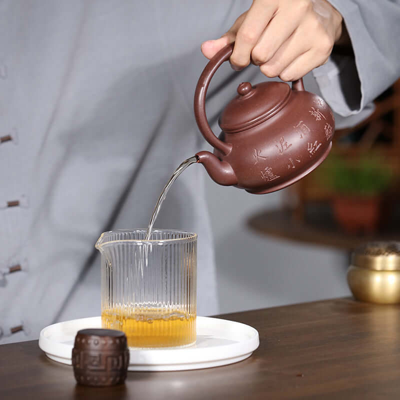 Handmade Yixing purple sand teapot pouring tea into a glass cup, showcasing traditional Kung Fu tea set craftsmanship.