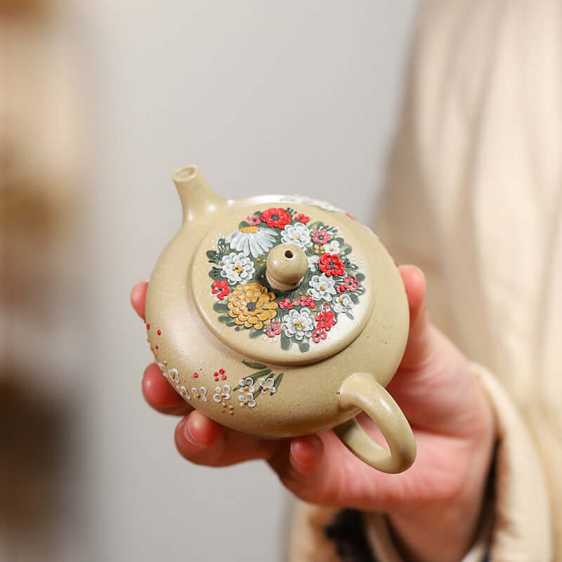 Handmade Yixing purple sand teapot with floral designs, held in hand, showcasing traditional craftsmanship.