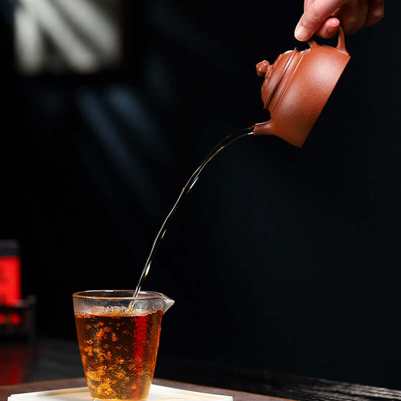 Handmade Yixing purple sand teapot pouring tea into a glass cup, showcasing traditional tea culture.