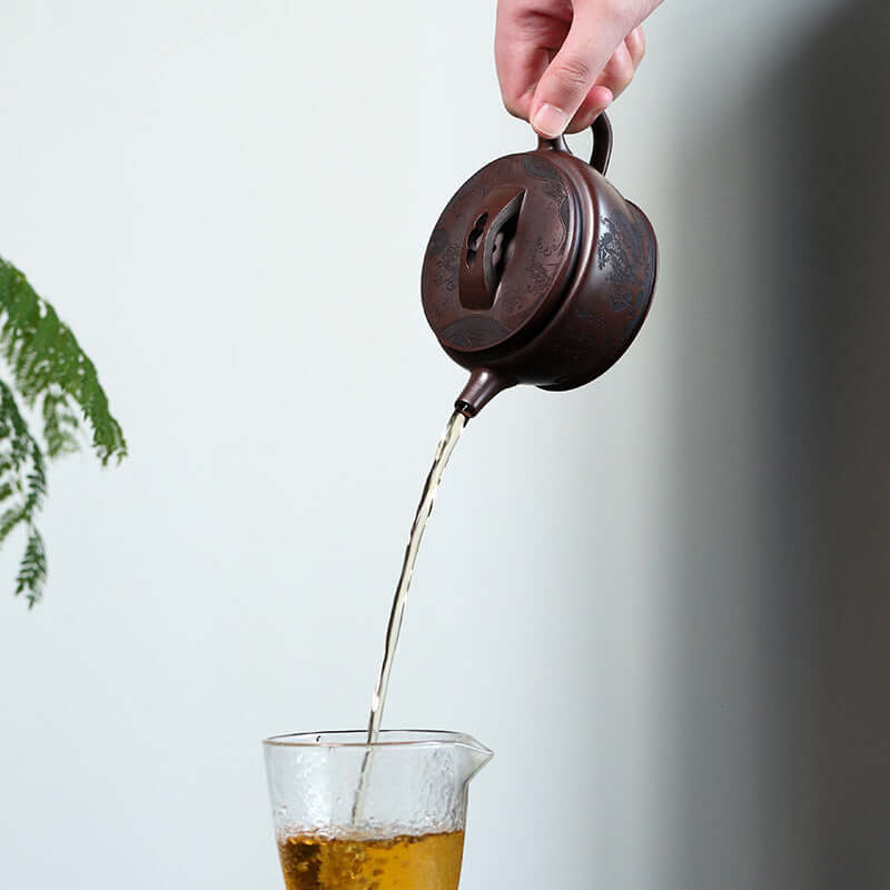 Handmade Yixing purple sand teapot pouring tea into a glass, showcasing traditional Chinese tea culture.