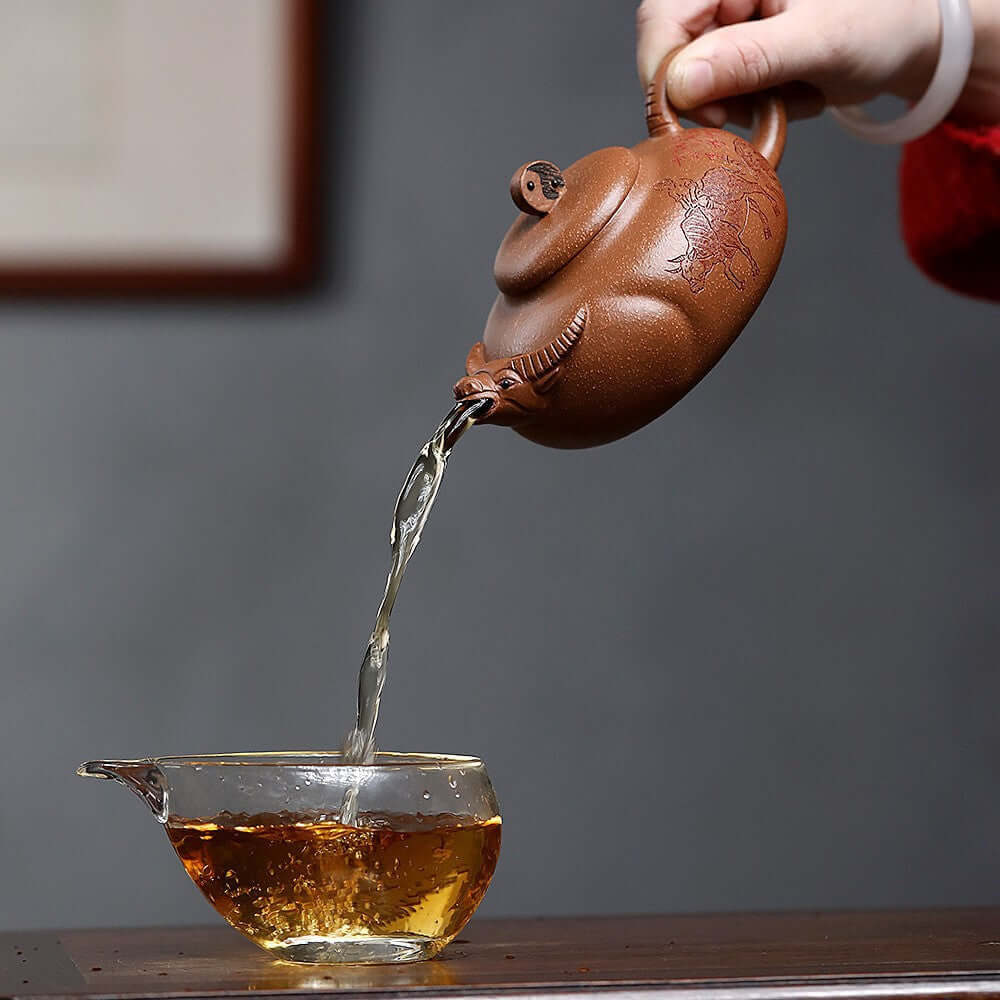 Handmade Yixing purple sand teapot pouring tea into a glass cup, showcasing traditional craftsmanship.