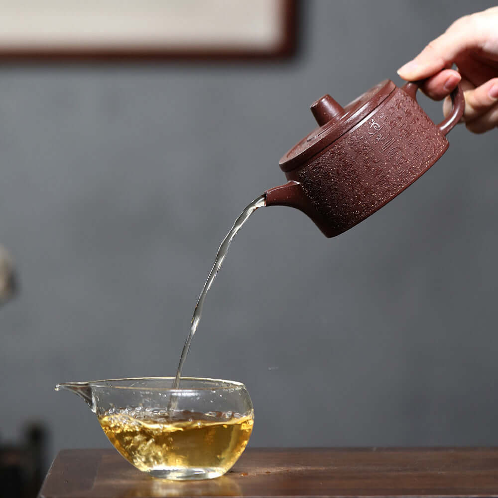 Handmade Yixing purple sand teapot pouring tea into a glass cup, perfect for home kung fu tea set.