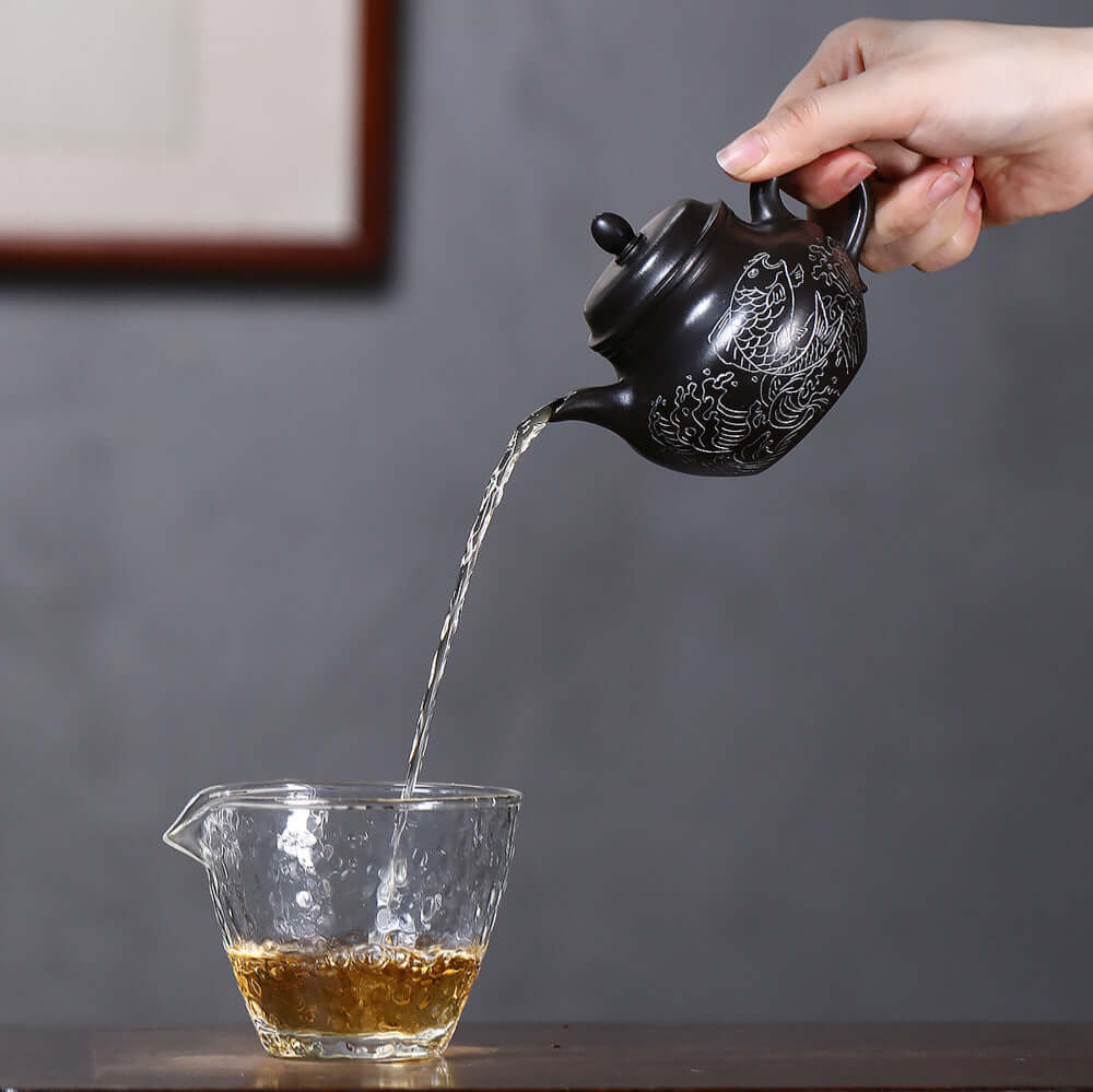 Handmade Yixing purple sand teapot pouring tea into a glass cup, featuring original Da Hong Pao design and craftsmanship.