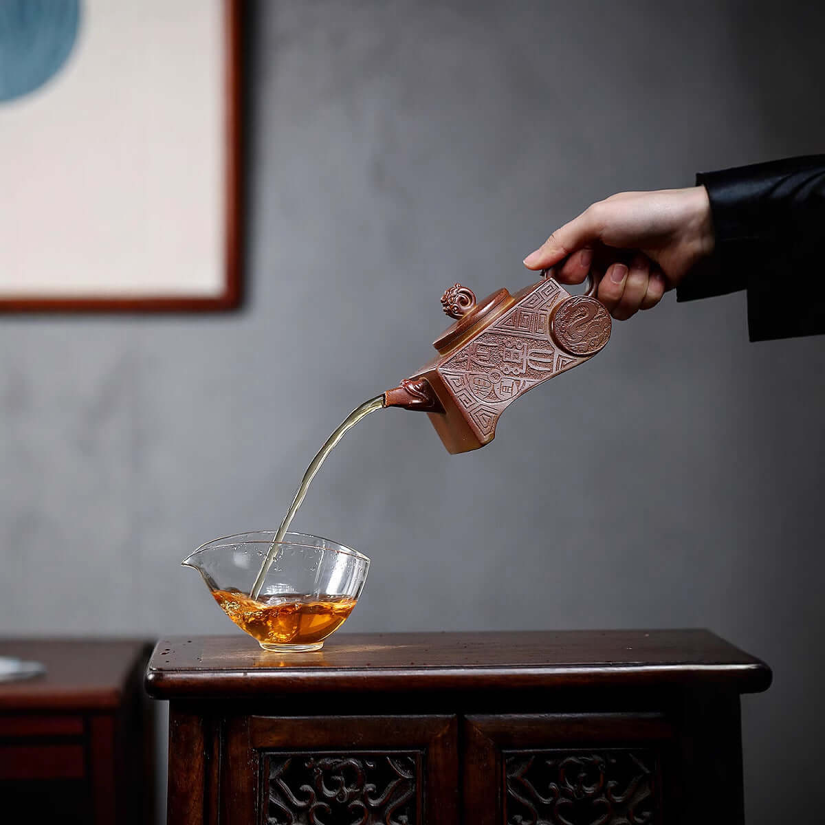 Handmade Yixing purple sand teapot pouring tea into a glass bowl, showcasing traditional craftsmanship.