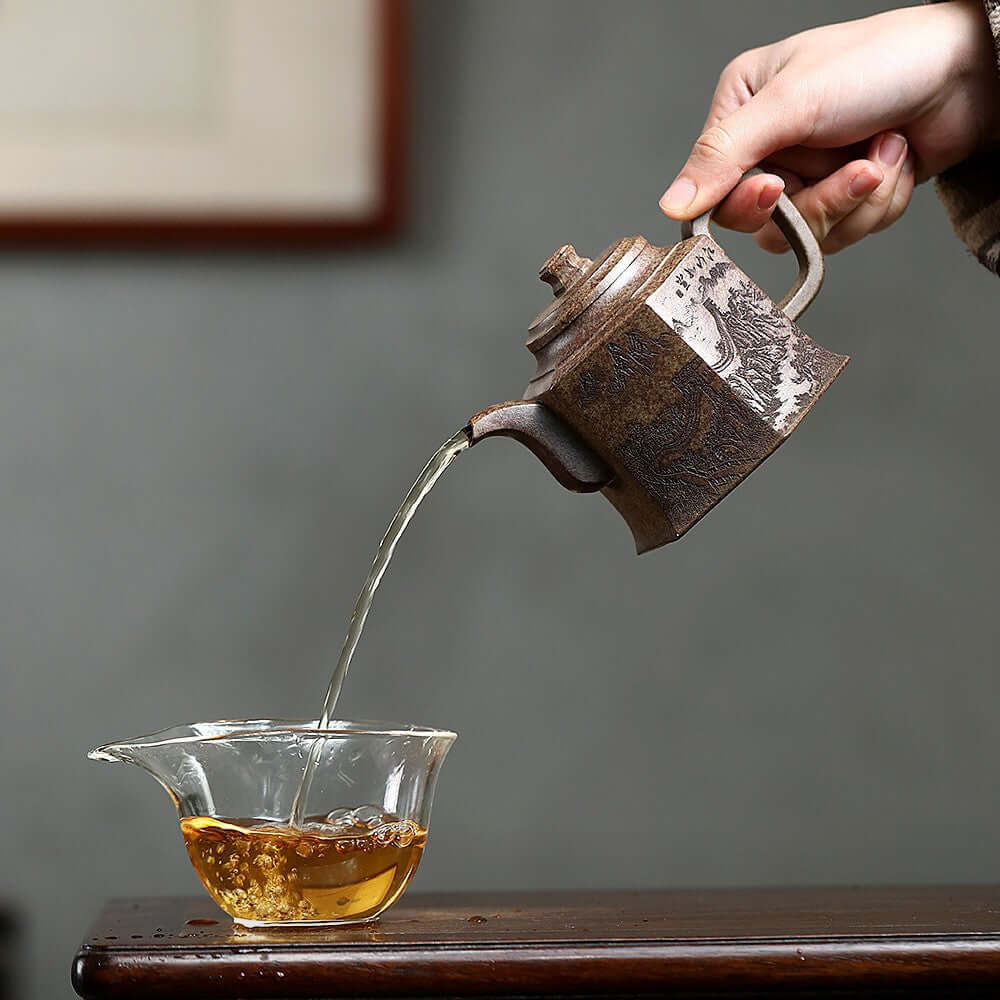 Hand pouring tea from a handmade Yixing purple sand teapot into a glass cup, showcasing traditional Kung Fu tea set.