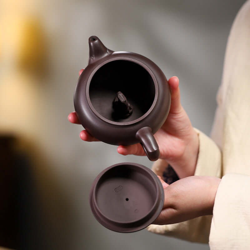 Handmade Yixing purple sand teapot held open showing interior design and lid, emphasizing craftsmanship and traditional style.
