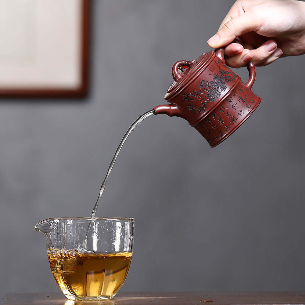 Handmade Yixing purple sand teapot pouring tea into a glass cup, showcasing the original craftsmanship and style.