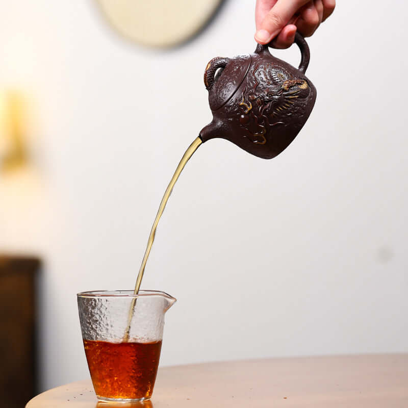 Handmade Yixing purple sand teapot pouring tea into a glass cup, showcasing traditional craftsmanship and rich tea color.