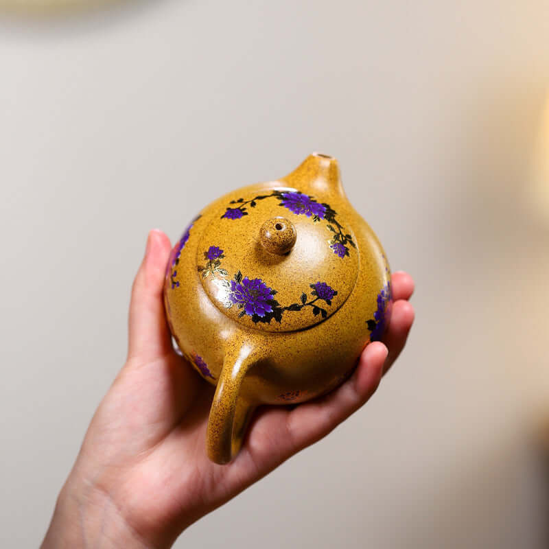 Handmade Yixing purple sand teapot featuring floral design, being held in a hand, showcasing its unique craftsmanship.