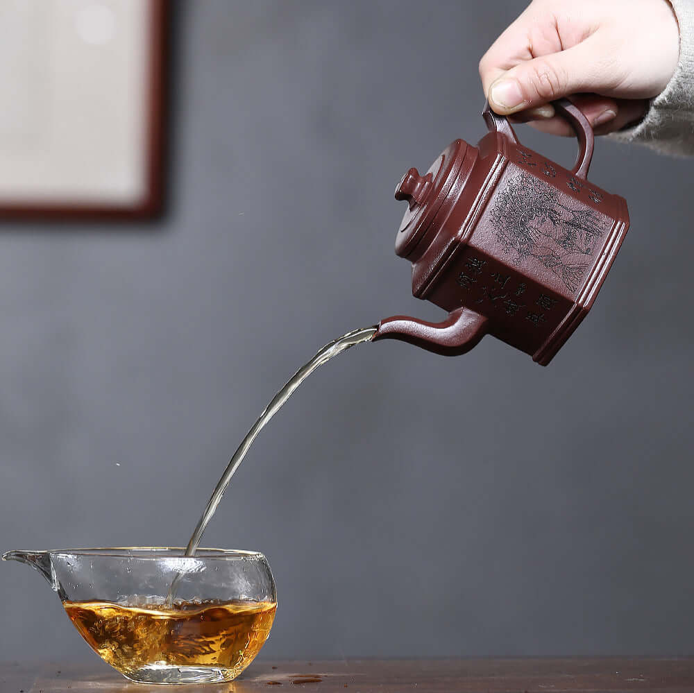 Handmade Yixing purple sand teapot pouring tea into a glass cup, showcasing craftsmanship and elegant design.