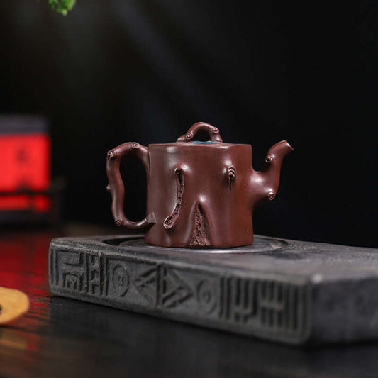 Handmade Yixing purple sand teapot with bionic tree stump design on a stone tea tray.