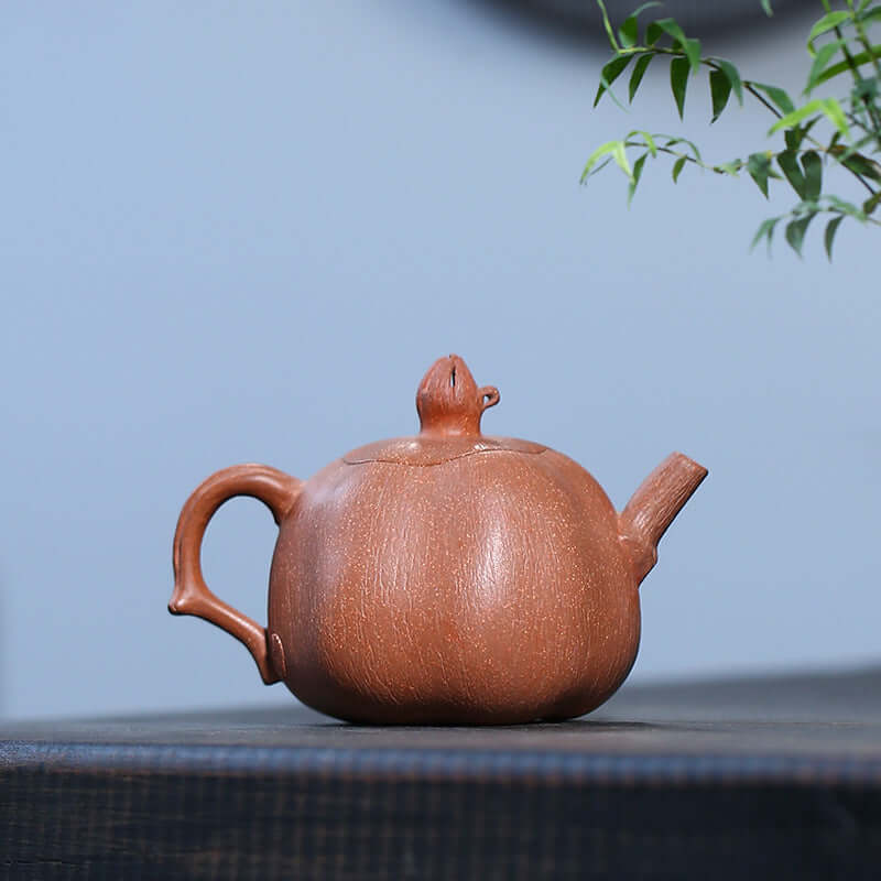 Handmade Yixing purple sand teapot shaped like a pomegranate, showcasing unique craftsmanship and natural clay texture.
