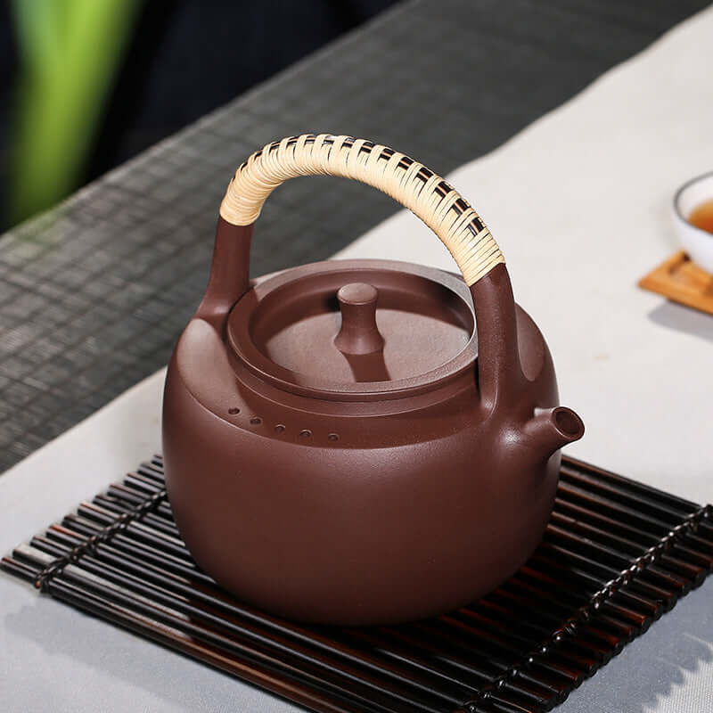 Handmade Yixing purple sand teapot with bamboo handle, ideal for brewing tea, high-temperature resistant, elegant design.