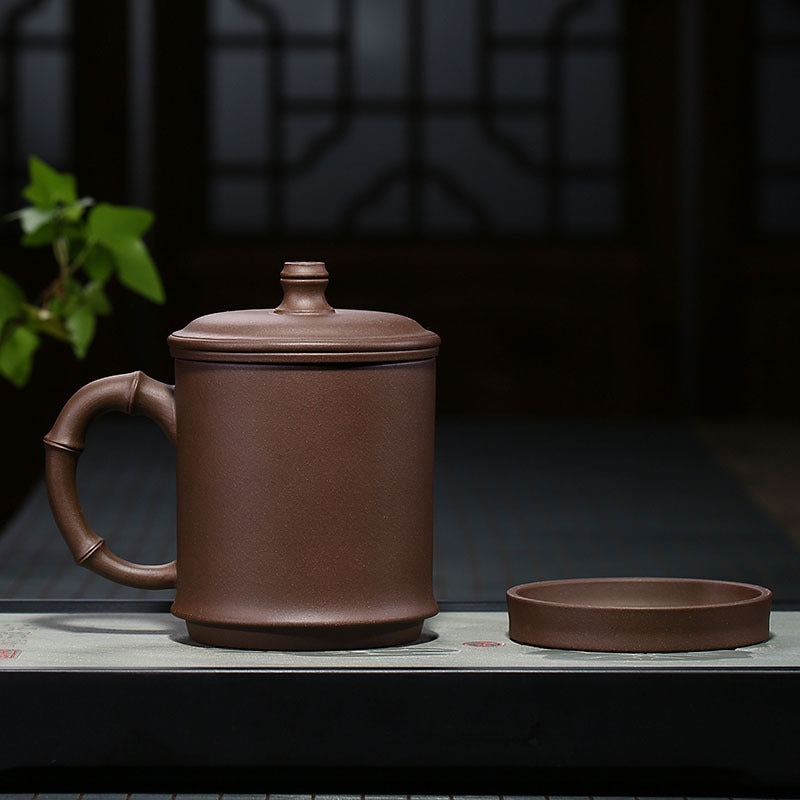 Handmade Yixing purple sand teapot with bamboo joint handle and matching lid on a tea table.