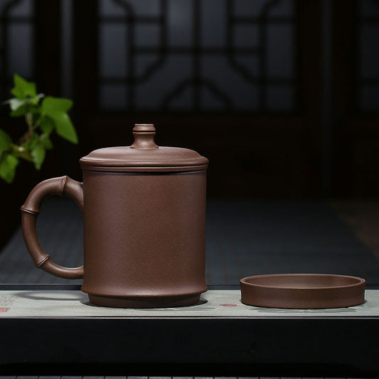 Handmade Yixing purple sand teapot with bamboo joint handle and matching lid on a tea table.
