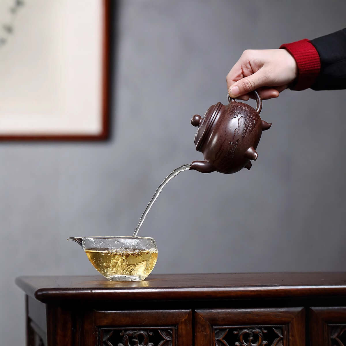 Handmade Yixing purple sand teapot pouring tea into a glass cup, showcasing traditional craftsmanship and elegance.