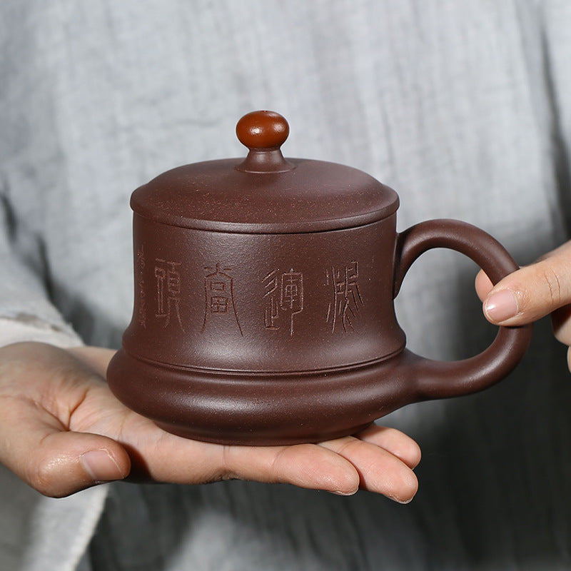 Handmade Yixing purple sand cup with a lid, held in hand, featuring intricate carvings and a round knob, 400ml capacity.