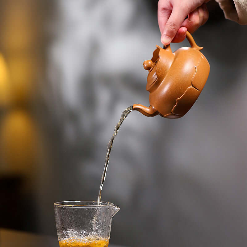 Handmade Yixing purple sand teapot pouring tea into a glass cup, showcasing traditional Kung Fu tea preparation.