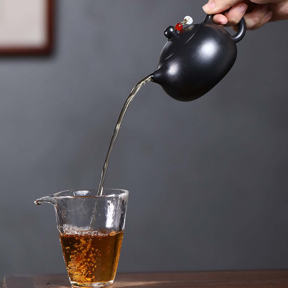 Handmade Yixing purple sand teapot pouring tea into a glass cup, showcasing elegant Kung Fu tea culture.