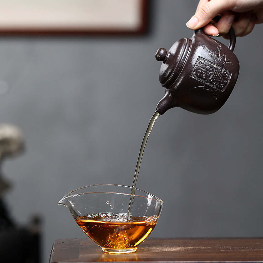 Handmade Yixing purple sand teapot pouring tea into a glass cup, showcasing the elegance of kung fu tea set.
