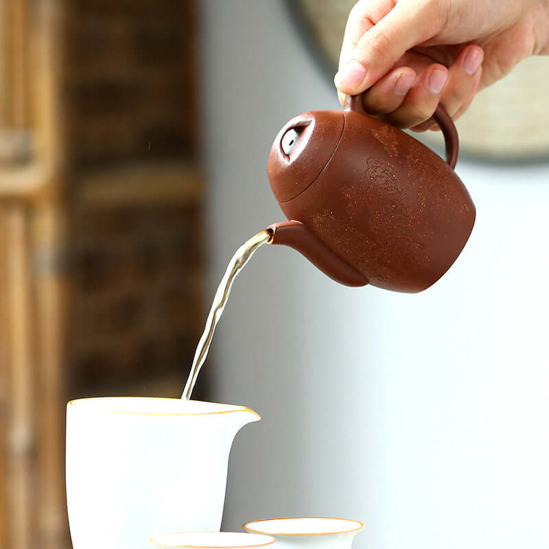 Hand pouring tea from a handmade Yixing purple sand teapot into a white teacup, showcasing traditional kung fu tea set.